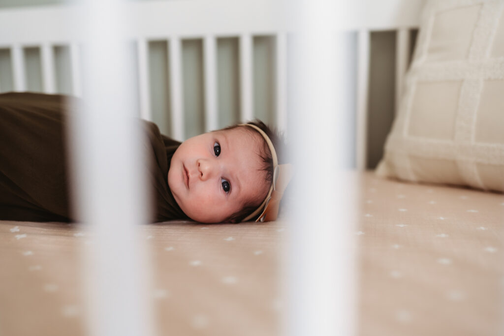 Baby girl peeking out of crib bars