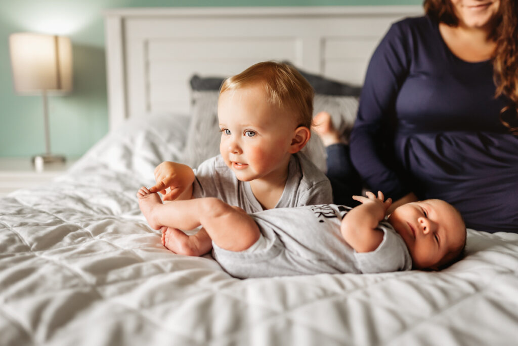 Little boy playing with newborn's toes on bed