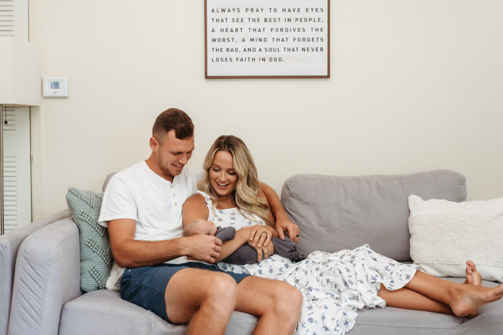 Mom and Dad holding newborn baby boy on couch in home